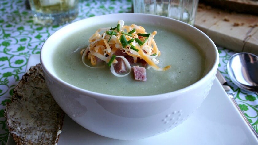 Bowl of potato soup garnished with chopped ham grated cheese and chives feature image